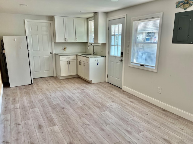 kitchen with light wood finished floors, a sink, freestanding refrigerator, electric panel, and light countertops