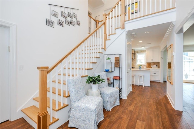 stairway with wood finished floors and crown molding