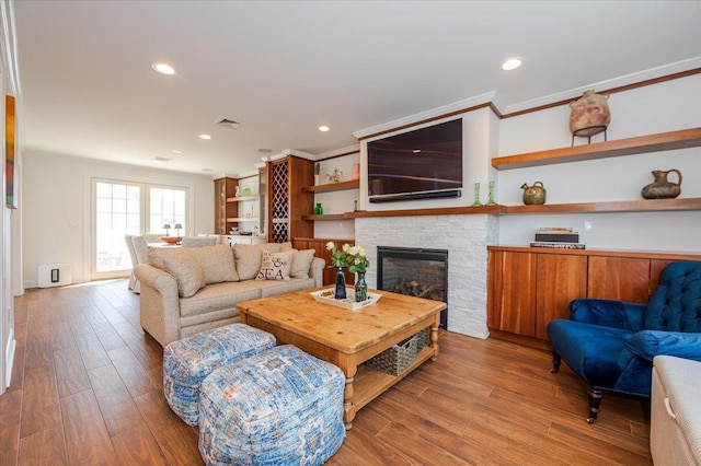 living room featuring recessed lighting, wood finished floors, and a stone fireplace