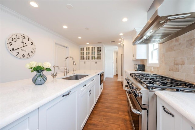 kitchen featuring a sink, high end range, decorative backsplash, wall chimney range hood, and ornamental molding
