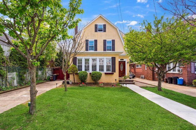 dutch colonial with stucco siding, fence, a front lawn, and a gambrel roof