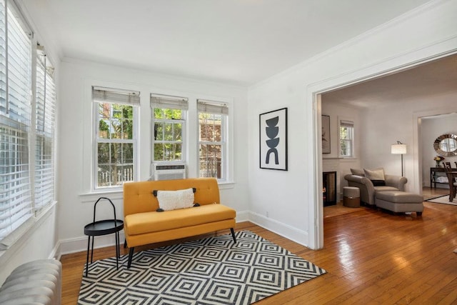 living area with baseboards, a warm lit fireplace, radiator, ornamental molding, and light wood-style flooring