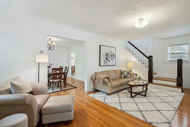 living area featuring a notable chandelier, a textured ceiling, baseboards, wood finished floors, and stairway