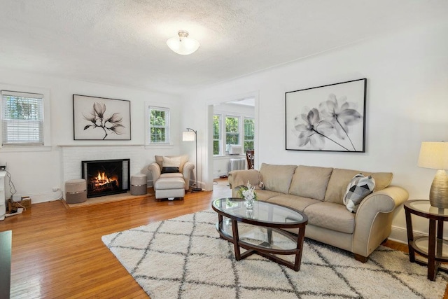 living area featuring baseboards, a brick fireplace, and wood finished floors