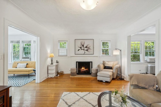 living room featuring light wood finished floors, a brick fireplace, radiator heating unit, and a healthy amount of sunlight