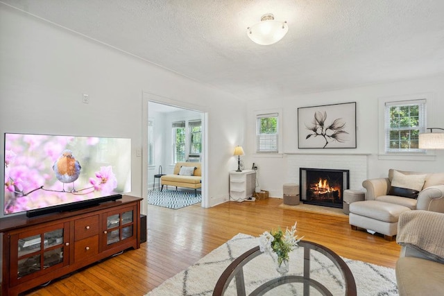 living room with a brick fireplace, a textured ceiling, a healthy amount of sunlight, and light wood finished floors