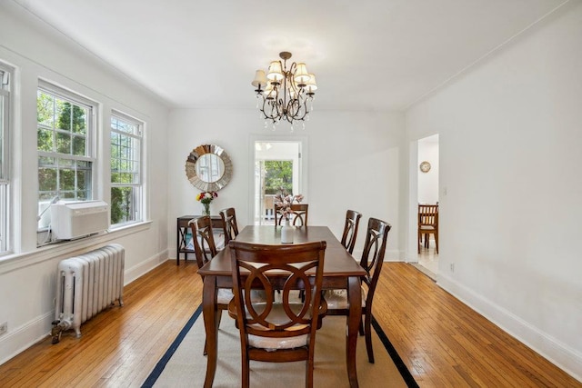 dining room featuring baseboards, radiator heating unit, light wood-type flooring, cooling unit, and a chandelier