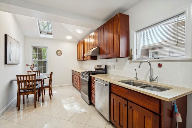 kitchen with appliances with stainless steel finishes, a sink, baseboards, light countertops, and under cabinet range hood
