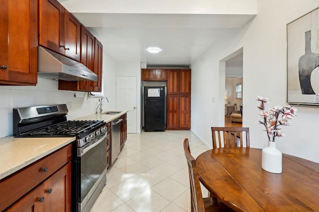 kitchen with light countertops, under cabinet range hood, a sink, appliances with stainless steel finishes, and light tile patterned floors