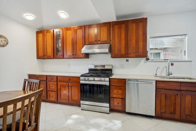 kitchen featuring a sink, light countertops, stainless steel appliances, under cabinet range hood, and glass insert cabinets