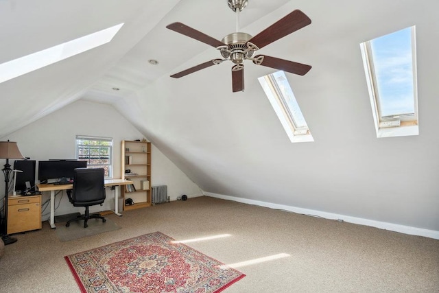 carpeted office featuring radiator, ceiling fan, and lofted ceiling with skylight