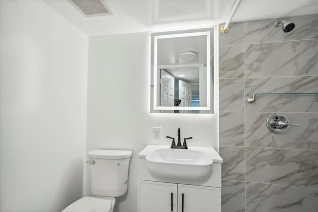 full bathroom featuring toilet, visible vents, tiled shower, and vanity