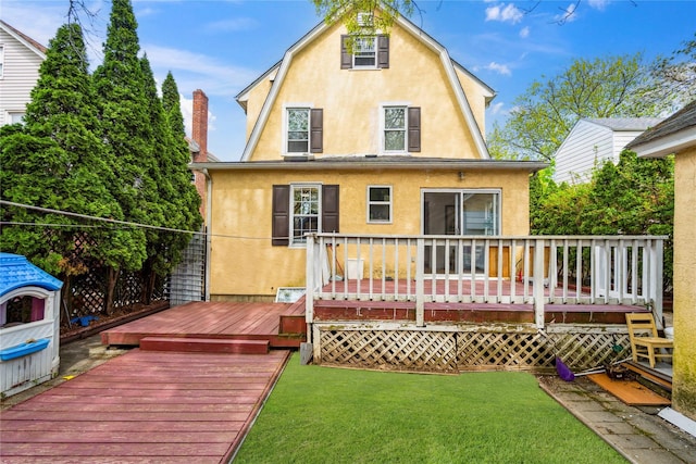 rear view of property featuring a gambrel roof, stucco siding, a yard, and a wooden deck