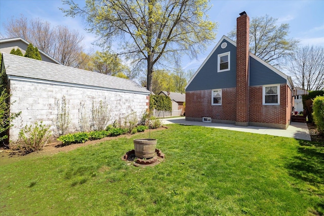 rear view of house featuring a chimney, fence, brick siding, a lawn, and a patio