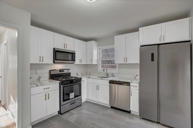 kitchen with light stone countertops, a sink, white cabinets, and appliances with stainless steel finishes