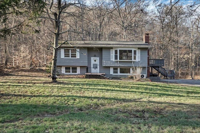 split foyer home with a wooded view, a wooden deck, a chimney, stairway, and a front lawn