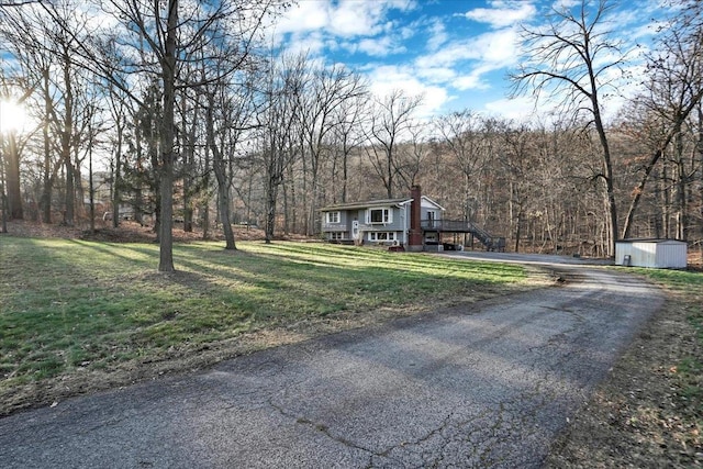 view of front facade featuring stairway, an outbuilding, aphalt driveway, a shed, and a chimney