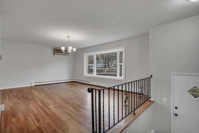 unfurnished room with a chandelier, a wall mounted air conditioner, baseboards, wood finished floors, and a baseboard radiator