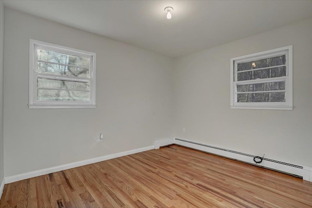 unfurnished room with wood finished floors, baseboard heating, and baseboards