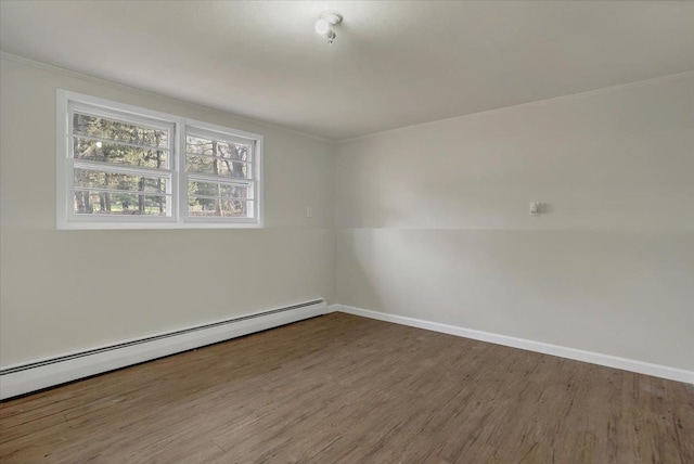 spare room featuring wood finished floors, crown molding, baseboard heating, and baseboards