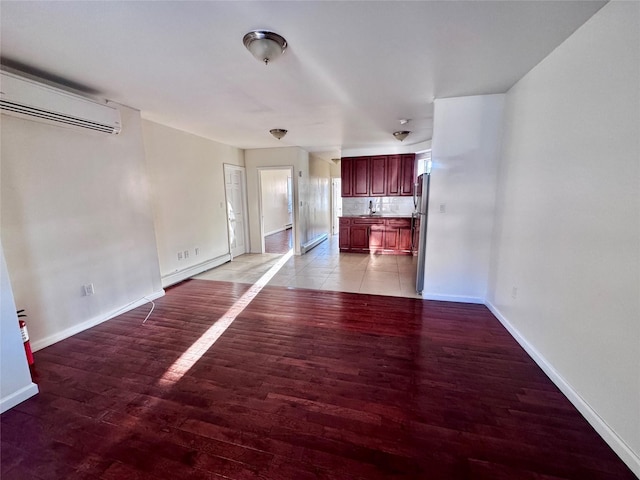 unfurnished living room featuring a wall mounted air conditioner, light wood finished floors, baseboards, and baseboard heating