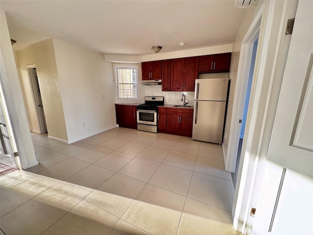 kitchen with a sink, reddish brown cabinets, stainless steel range with gas stovetop, under cabinet range hood, and freestanding refrigerator