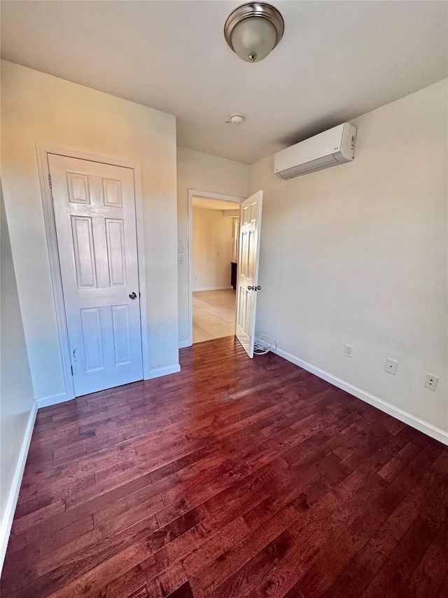 unfurnished bedroom with a wall mounted AC, baseboards, and dark wood-style flooring