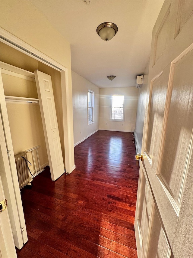 unfurnished bedroom featuring wood-type flooring, a wall mounted AC, a closet, and baseboards
