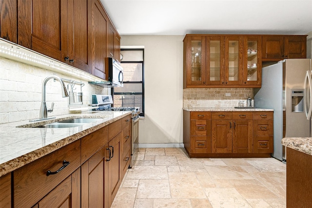 kitchen featuring a sink, brown cabinetry, stone tile flooring, backsplash, and appliances with stainless steel finishes