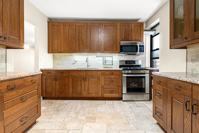 kitchen with stainless steel appliances, tasteful backsplash, a sink, and stone tile flooring