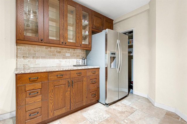 kitchen with glass insert cabinets, baseboards, brown cabinetry, stainless steel fridge, and decorative backsplash