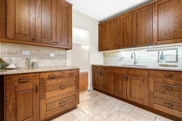 kitchen featuring a sink, brown cabinetry, decorative backsplash, and baseboards