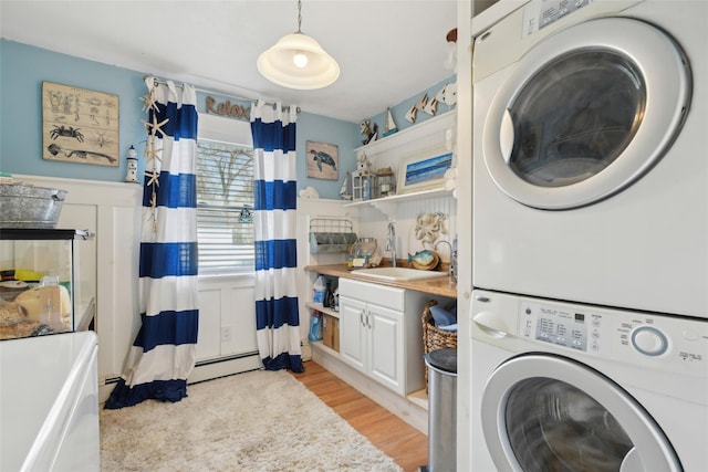 clothes washing area with a sink, light wood-style floors, laundry area, a wainscoted wall, and stacked washer and dryer