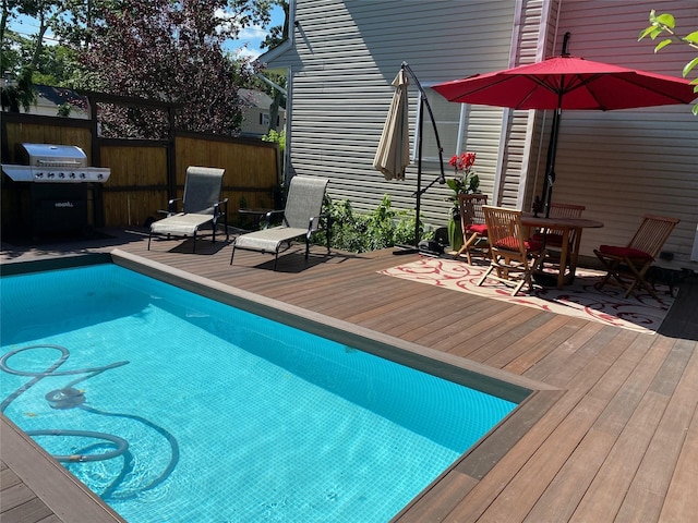 view of pool featuring a deck, grilling area, fence, a fenced in pool, and outdoor dining space