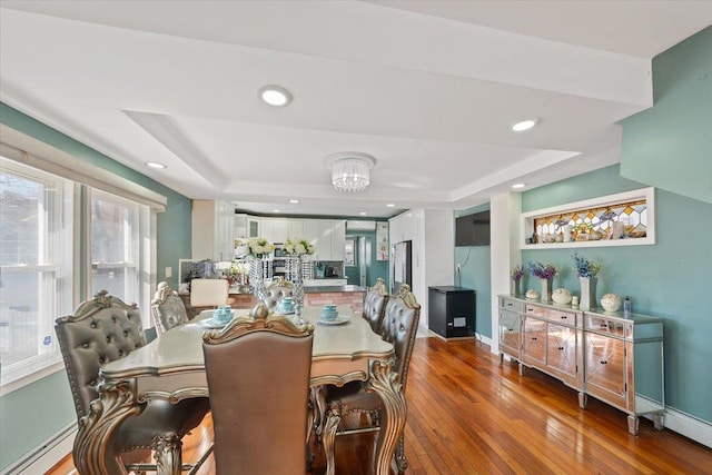 dining room with baseboards, hardwood / wood-style flooring, a tray ceiling, and recessed lighting