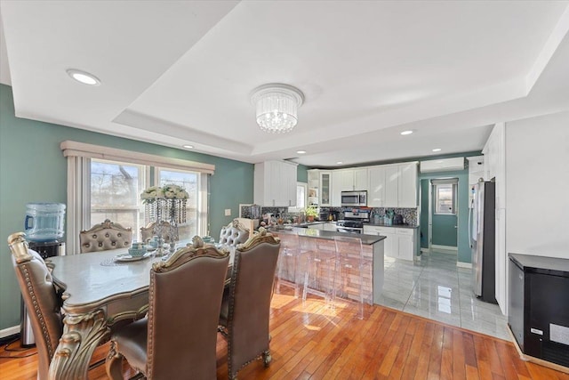 dining space with an inviting chandelier, a tray ceiling, light wood-type flooring, and a wealth of natural light