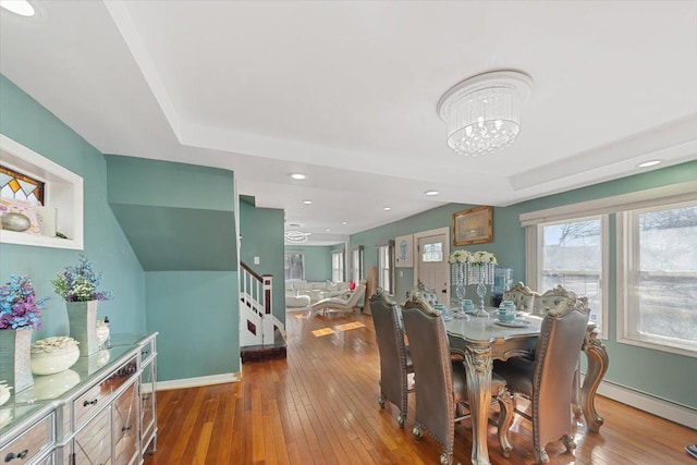 dining space with stairway, a raised ceiling, wood-type flooring, baseboards, and a chandelier