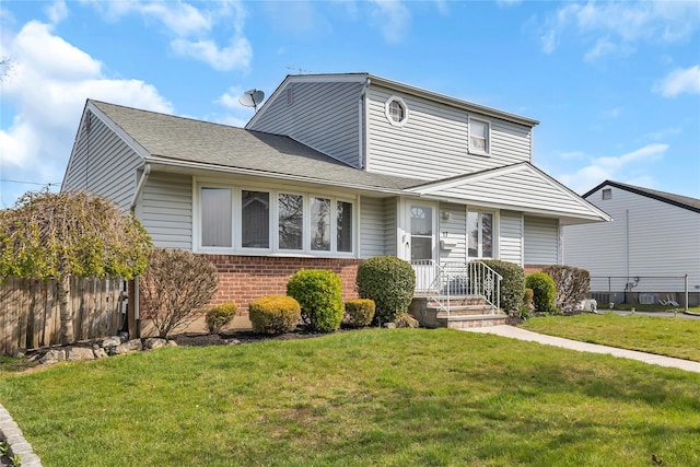 traditional home with fence, a shingled roof, a front yard, and brick siding