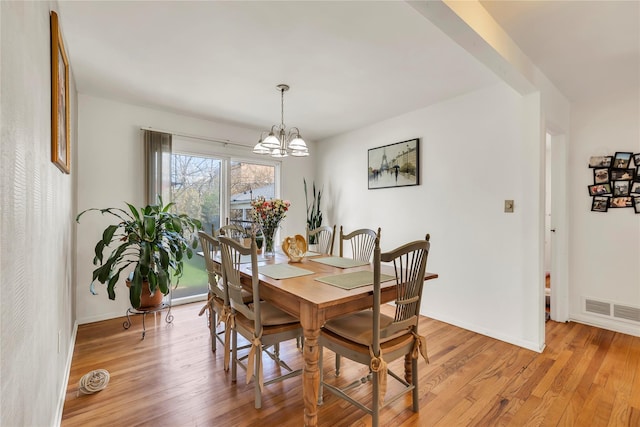 dining space with baseboards, visible vents, light wood finished floors, and a chandelier