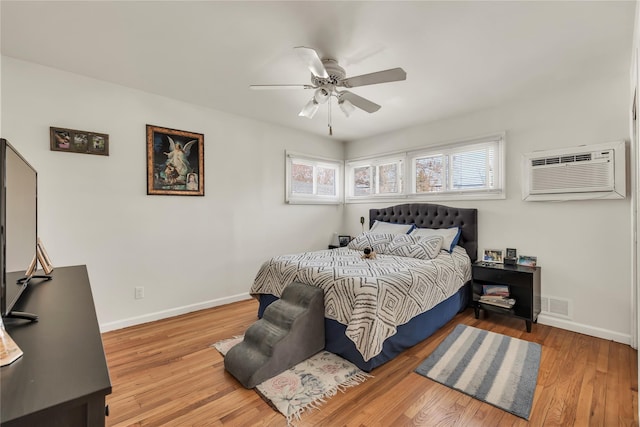 bedroom featuring a ceiling fan, visible vents, a wall mounted air conditioner, wood finished floors, and baseboards