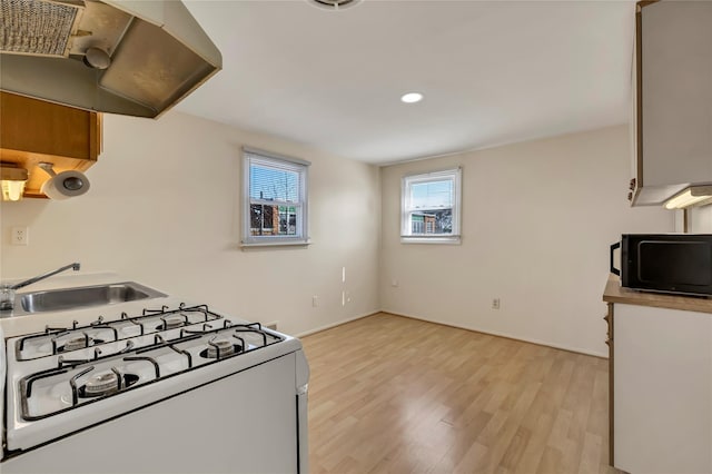 kitchen with black microwave, white range with gas stovetop, under cabinet range hood, a sink, and light wood finished floors