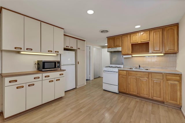 kitchen with white appliances, under cabinet range hood, a sink, and light wood-style flooring
