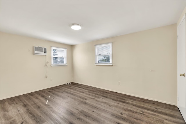 spare room with baseboards, a wall unit AC, and wood finished floors
