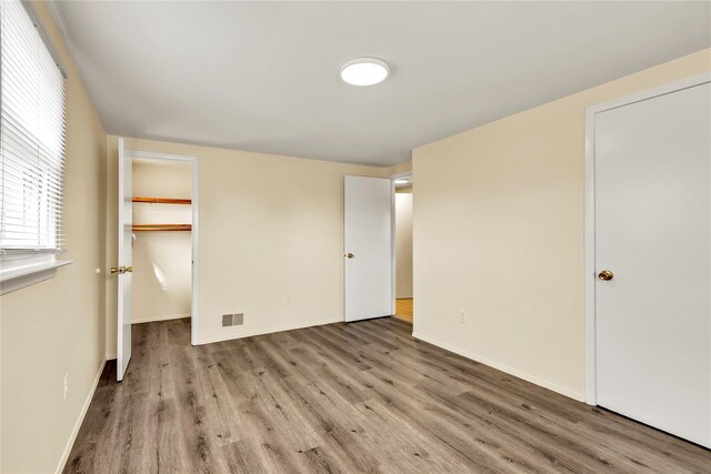 unfurnished bedroom featuring visible vents, baseboards, a walk in closet, and wood finished floors