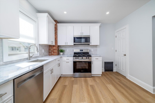 kitchen with stainless steel appliances, a sink, light wood finished floors, and tasteful backsplash