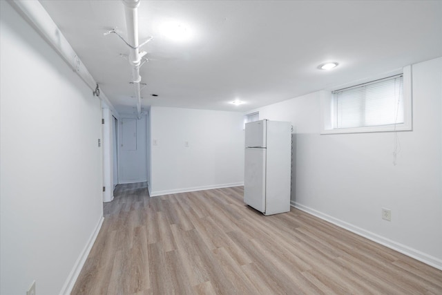 basement with baseboards, freestanding refrigerator, and light wood-type flooring