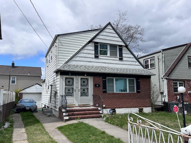 bungalow-style house with roof with shingles, fence, brick siding, a garage, and an outbuilding