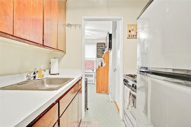 kitchen with freestanding refrigerator, a sink, stainless steel range with gas stovetop, light countertops, and light flooring