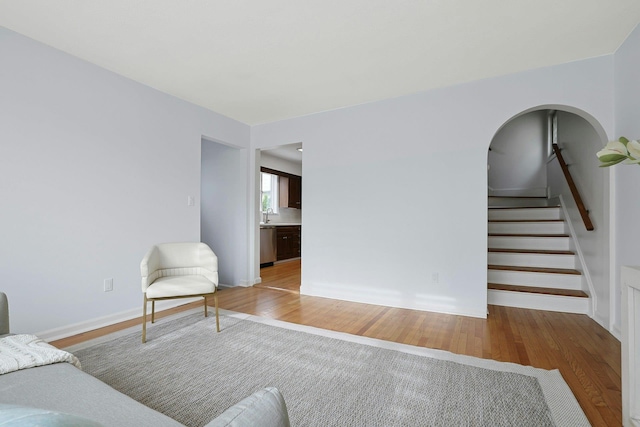 living area with baseboards, arched walkways, stairs, and light wood finished floors