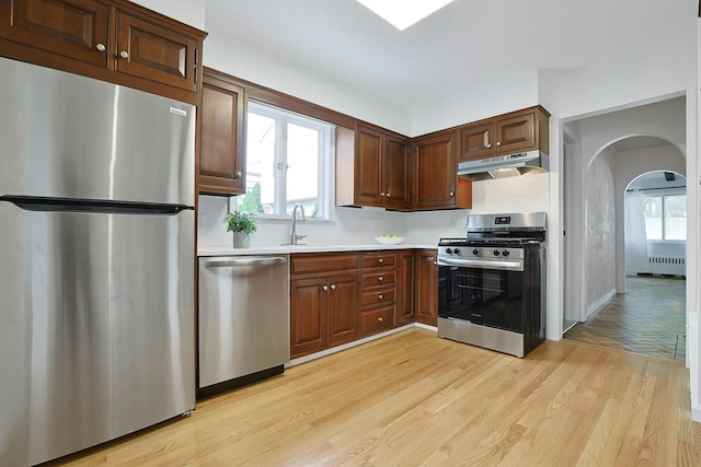 kitchen featuring arched walkways, light wood-style flooring, under cabinet range hood, appliances with stainless steel finishes, and light countertops